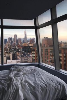 an unmade bed in front of large windows overlooking the city