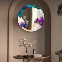 a round mirror hanging on the side of a wall next to a table with flowers