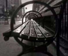 an empty park bench is seen through the reflection of it's metal armrests