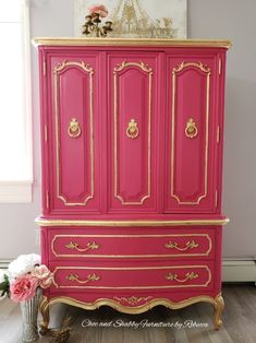 a pink and gold painted armoire next to a vase with flowers on it in a room