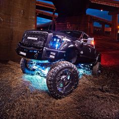 a black truck parked under a bridge with its lights on and the front wheels off