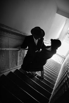 black and white photograph of a woman walking up the stairs wearing a suit and hat