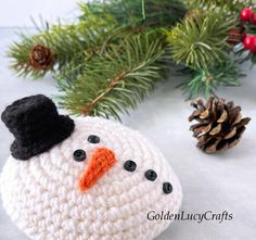 a crocheted snowman ornament next to pine cones