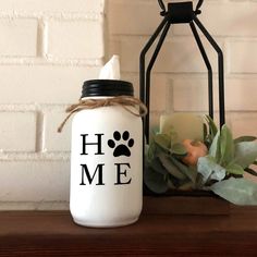 a white jar sitting on top of a wooden table next to a candle and potted plant