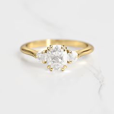 a three stone diamond ring on a white marble surface, with the center setting in yellow gold