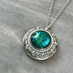 XL Antiqued Silver Brass Locket with Large Round Blue Green Glass Cabochon...  This locket is absolutely beautiful and looks even better in person!  I made this locket necklace with an XL antiqued silver plated brass locket.  In the center of the locket, I attached an antiqued silver plated filigree and a beautiful round blue green glass cabochon to the center of the filigree.  This statement locket will hold two photos. The antiqued silver plated brass chain is a soldered non-tarnish chain and it closes with a lobster claw clasp.  The chain may vary due to supply shortages but will be a high quality non-tarnish and soldered chain Locket - 1.73" in diameter (44mm in diameter)  Interior photo area - 30-31mm approx.  This fabulous statement locket will be sent to you gift wrapped in a beauti Luxury Medallion Cabochon Jewelry, Luxury Cabochon Necklace For Women, Luxury Silver Cabochons, Chain Locket, Locket Vintage, Photo Area, Victorian Locket, Animal Brooch, Photo Locket