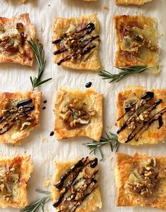 small crackers topped with nuts and rosemary on a sheet of parchment paper, ready to be eaten