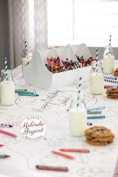 a table topped with cookies and milk next to two cups filled with colored crayons