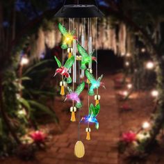 a colorful wind chime hanging from a tree with lights in the background and flowers on it