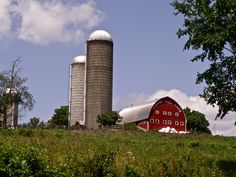 a large red barn sitting on top of a lush green hillside next to a tall silo