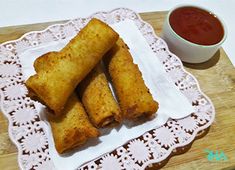 some fried food on a white plate next to a cup of sauce and a spoon