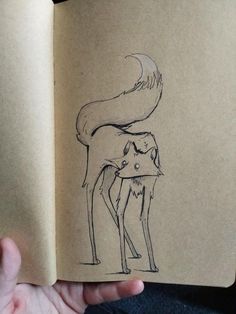 a hand holding an open book with a drawing of a fox on it's back