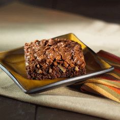 a brownie on a yellow plate sitting on top of a table next to a napkin