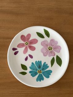 a plate with flowers painted on it sitting on top of a wooden table next to a knife and fork