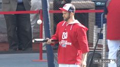 a man holding a baseball bat in front of a fence with other people behind him