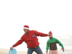 two men playing frisbee on the beach in santa hats and green sweaters