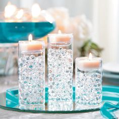 three candles sitting on top of a blue plate next to white flowers and glass vases