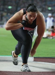 a woman in black and white running on a track with her hands behind her head