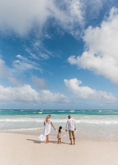 a man and woman holding hands while walking on the beach with a small child in front of them