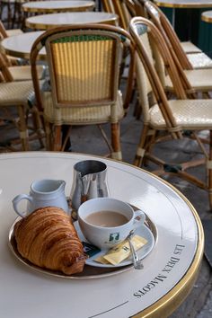 there is a croissant and coffee on the table in front of some chairs