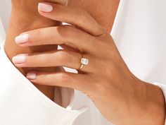 a woman's hand wearing a gold ring with a diamond in the middle and a white background