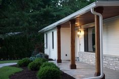 an outside view of a white house with wood columns and lights on the side of it