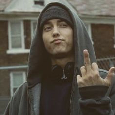 a man in a hoodie making the peace sign with his hand while standing next to a house