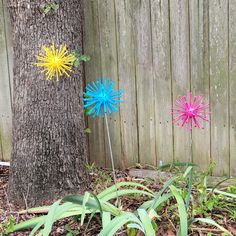 two brightly colored pinwheels next to a tree in front of a wooden fence