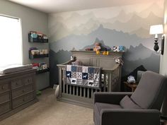 a baby's room with mountains painted on the wall and a crib in the foreground