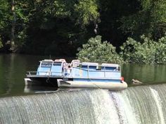 a boat that is sitting in the water near a dam with trees behind it and another boat on the side of the river