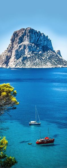 two boats floating in the blue water near an island