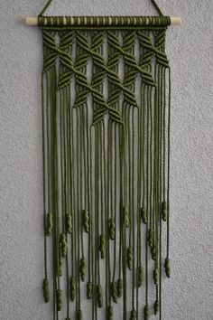 a wall hanging made out of green string and wood sticks with beads attached to it