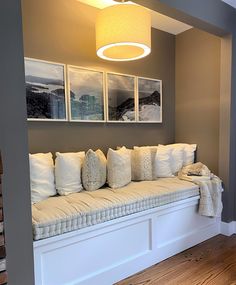 a white couch with pillows on it in front of a window and pictures hanging above