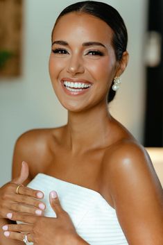 a woman in a white dress smiling and holding onto her wedding ring with one hand