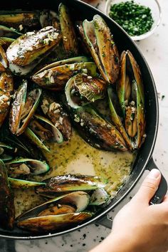 someone is cooking mussels in a pan on the stove with garlic and parsley