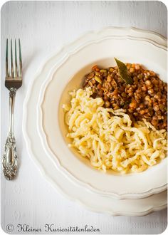 a white bowl filled with pasta and meat on top of a table next to a fork