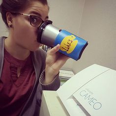 a woman drinking from a coffee cup in front of a computer desk with books on it