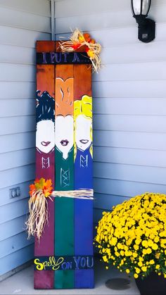 a colorful wooden sign sitting on the side of a building next to flowers and a potted plant