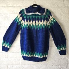 a blue sweater with green and white designs hanging from a hook on a brick wall