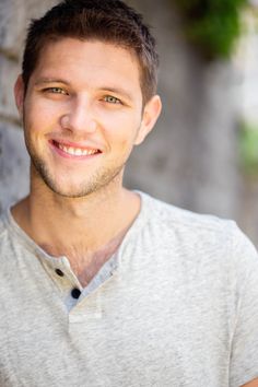 a young man is smiling and posing for the camera in front of a stone wall