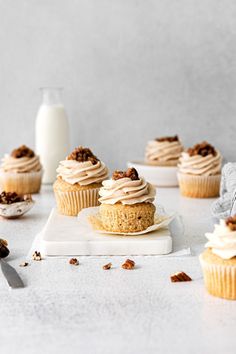 several cupcakes with frosting and nuts on a cutting board next to a glass of milk