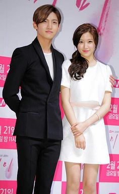 two people standing next to each other in front of a pink and white wall at an event