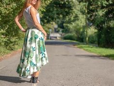 a woman standing on the side of a road wearing a skirt and smiling at the camera