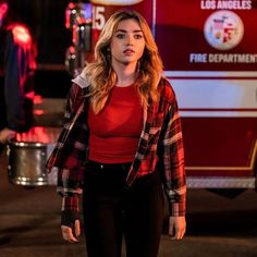 a woman standing in front of a firetruck with her hand on her hip