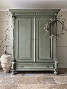 a green armoire sitting on top of a tiled floor next to a potted plant