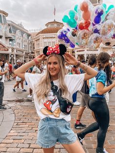 a woman in mickey mouse ears is posing for the camera with balloons floating over her head