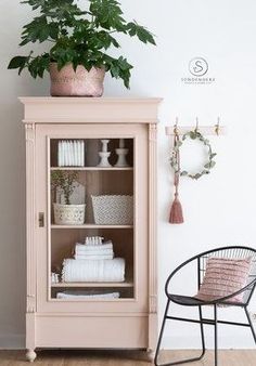 a pink cabinet sitting next to a chair and potted plant on top of it