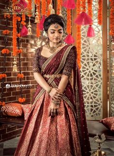 a woman in a maroon and gold lehenga with orange tassels hanging from the ceiling