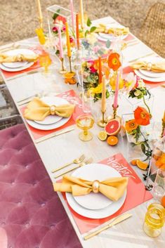 the table is set with yellow and pink plates, napkins, and orange flowers