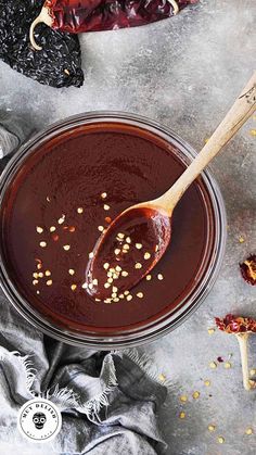 a spoon full of sauce sitting on top of a table next to some dried herbs